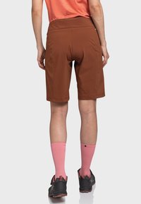 Braune Shorts mit lockerer Passform, aus Stretchgewebe gefertigt. Getragen mit pinken knielangen Socken und schwarzen Sportschuhen.