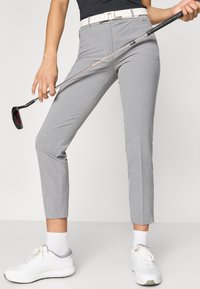 Γκρίζα κολάν έχουν κομψή εφαρμογή, λεία υφή και μήκος ως τον αστράγαλο με μια ελαφριά σχισμή στο στρίφωμα, συνδυασμένα με μια λευκή ζώνη και αθλητικά παπούτσια.