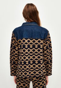 Jeansjacka med en mörkblå krage, med ett mönstrat design i nyanser av beige och marinblått, med intrikata geometriska former och texturer.