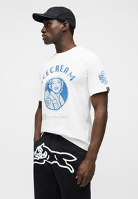 Λευκό βαμβακερό t-shirt με μπλε γραφικό εκτύπωμα μιας γυναίκας και το κείμενο "ICE CREAM". Μαύρο τζιν παντελόνι με λευκό σχέδιο σιλουέτας σκύλου.