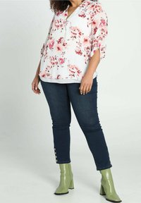 Blusa a stampa floreale bianca, con fiori rosa e rossi, caratterizzata da un ampio scollo e maniche a tre quarti. Paio di jeans skinny scuri con dettagli a bottoni.