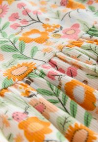 Lilleline puuvillakangas, millel on oranži, roosa ja rohelise mustriga volditud tekstuur ja ribadega detailid, esitleb päevalilli ja söögimardikaid.