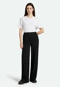 White short-sleeve t-shirt paired with black wide-legged pants featuring a textured ribbed pattern. Black platform shoes complete the look.