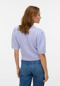 Lila pletena jopica s kratkimi pufastimi rokavi, teksturirano, mehko blago; v kombinaciji z modrimi kavbojskimi hlačami z visokim pasom, pogled od zadaj.