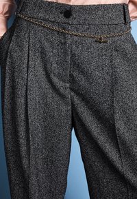 High-waisted gray herringbone trousers with black button and gold chain belt over pink satin blouse against blue background.