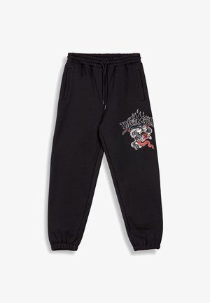 Zwarte joggingsbroek met een elastische tailleband en boorden, voorzien van zijzakken. Een decoratieve graphic van een draak en vlammen op het linkerbeen.