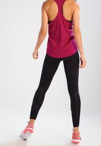 Zwarte sportlegging met textuuraccenten, gecombineerd met een mouwloze magentakleurige top. De outfit heeft een racerback ontwerp en lichte sportschoenen.