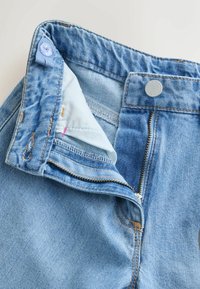 Blugi din denim albastru deschis cu fermoar deschis, nasture metalic vizibil și găură pentru nasture pe talie, pe un fundal simplu.