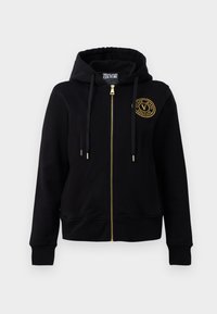 Black hooded sweatshirt with a gold zip and emblem. Features long sleeves, ribbed cuffs, and a drawstring hood. Soft fabric texture.