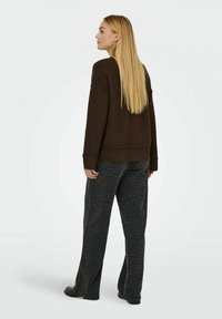 Maglione marrone a maglia con orlo a costine, abbinato a pantaloni grigi scuri con una discreta stampa leopardata, visti da dietro.