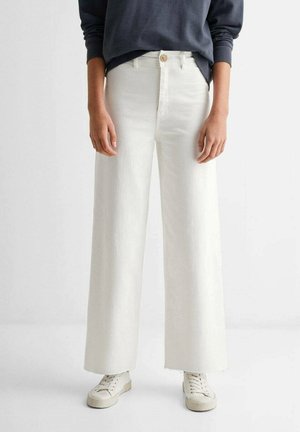 Jeans en denim blanc taille haute et coupe évasée avec un ourlet effiloché, doté d'une fermeture à un bouton et de poches avant. Associés à un haut foncé et des baskets.