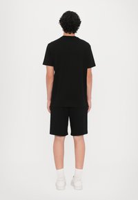 Svart bomulls t-skjorte med rund hals og korte ermer, kombinert med svarte bomullsshorts. Hvite joggesko med lav profil og hvite sokker.
