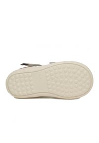 Witte rubberen schoenzool met een gestructureerde oppervlakte, voorzien van ronde bobbels voor grip en twee grijze suède banden voor een veilige pasvorm.