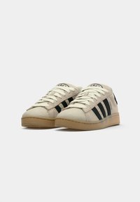 Beige suede sneakers with black stripes, cream laces, rounded toe, and gum rubber sole. Features logo on tongue and back heel.