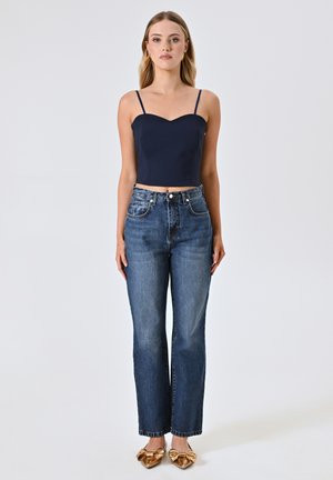 Crop top blu navy con spalline sottili, jeans blu a vita alta e ballerine dorate con dettaglio a fiocco. Tessuto morbido e vestibilità rilassata.