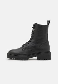 Black leather combat boot with lace-up front, chunky rubber sole, ankle height, and pull tab at the back on a plain white background.