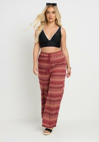 Svart bh med vita kantdetaljer, kombinerad med röda byxor med zigzag-mönster och svarta sandaler med platå.