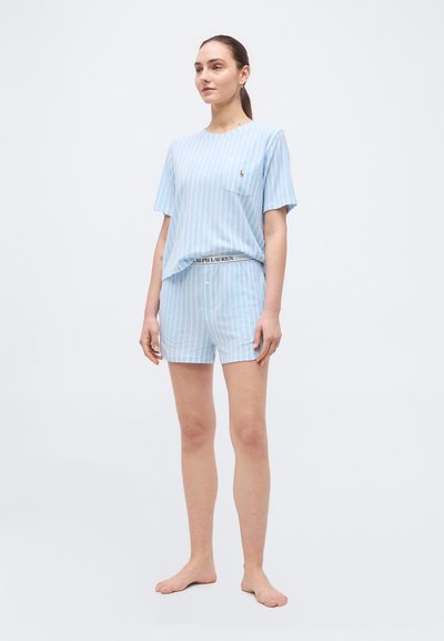 Γυναίκα που στέκεται ξυπόλητη, φορώντας μπλουζάκι κοντομάνικο με γαλάζιες και λευκές ρίγες και ταίριαστο σορτς με το λογότυπο της Ralph Lauren στη μέση και στην τσέπη.