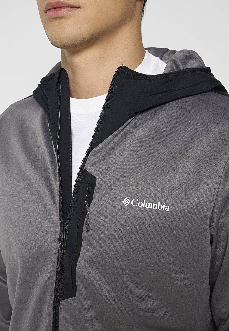 Graue Zip-Jacke mit schwarzer Kapuze. Enthält das Columbia-Logo, hat eine glatte Textur und sichtbare Reißverschlussdetails.