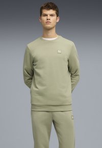 Lys grøn sweatshirt med rund hals og ribbede manchetter, der har et lille logo-patch på venstre bryst. Blød, glat tekstur.