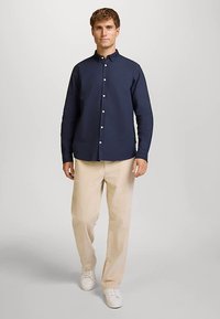 Marineblauw overhemdbloesje van een gladde stof, gecombineerd met lichtbeige corduroy broek en witte sneakers; de outfit heeft een klassieke kraag.