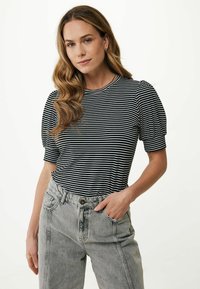 T-shirt a righe bianche e nere con maniche corte a sbuffo, scollo rotondo, abbinato a jeans chiari a vita alta con tasche frontali.