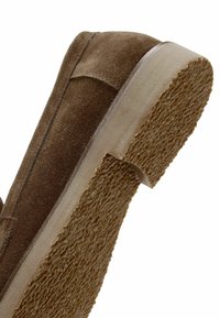 Bruine suède schoen met een gestructureerde rubberen zool. Heeft een laag profiel en een ronde neus. Zijnaadstiksels voegen ontwerpelementen toe.