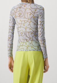 Vaaleansininen pitkähihainen paita, jossa on läpikuultava tekstuuri ja kultaketju- sekä riipuskuvio. Yhdistetty korkeavyötäröisiin keltaisiin housuihin.