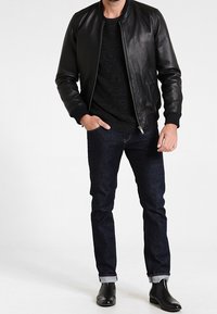 Svart läderbomberjacka med ribbad mudd, parat med en mörk stickad tröja och slim-fit jeans, avslutat med svarta ankelboots.