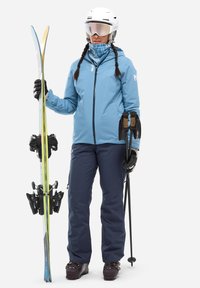 Ski gear featuring a light blue waterproof jacket, navy ski pants, black gloves, helmet, and ski gear including skis and poles.