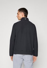 Suéter negro con cuello alto y tela texturizada. Presenta un logo blanco en el cuello y puños y dobladillo acanalados.
