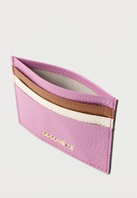 Skórzany etui na karty w jasnoróżowym kolorze, ozdobione dwoma brązowymi i jedną białą paskiem. Gładka faktura z złotym napisem na przodzie.