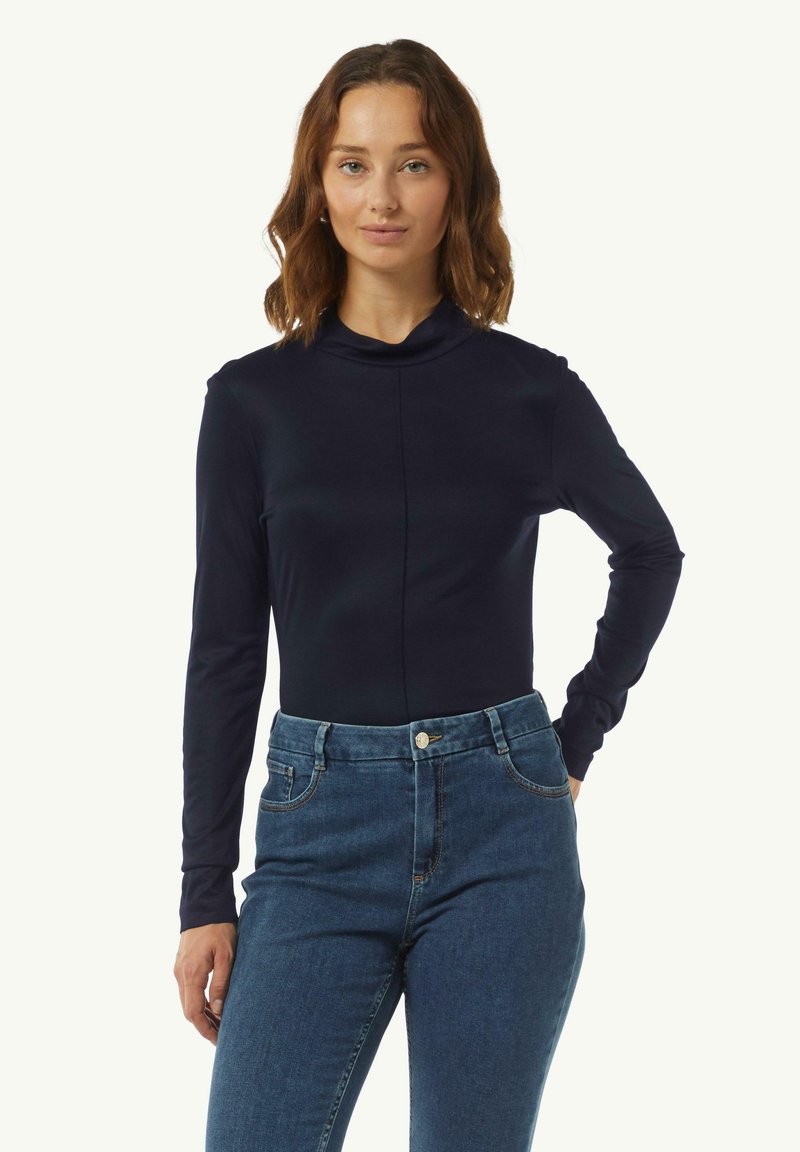 Marinefarbener Langarmoberteil mit Kragen, aus glattem Stoff. Kombiniert mit hochgeschnittenen blauen Jeans, die über vordere Taschen und einen Metallknopf verfügen.