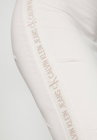 Bílé joggingové kalhoty s bočním panelem s textem "CALVIN KLEIN JEANS" v béžové barvě, vyrobené z materiálu s obsahem bavlny s hladkou strukturou.