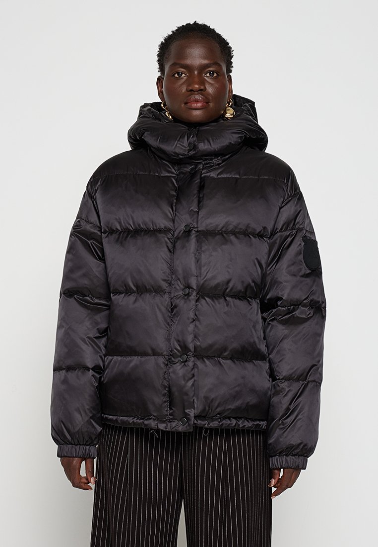 Schwarze Daunenjacke mit hochgeschlossenem Kragen, Knopfverschluss und elastischen Bündchen. Verfügt über genähte Steppabschnitte und ein Logo-Patch am Ärmel.