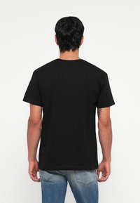 T-shirt en coton noir à manches courtes avec col rond, présentant une coupe droite et des détails de couture minimalistes, porté avec un jean bleu délavé.