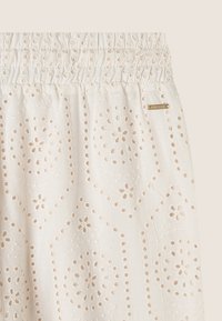 Tessuto di cotone bianco con motivi floreali ricamati e dettagli a intaglio, dotato di una vita arricciata e di un'etichetta metallica del marchio.