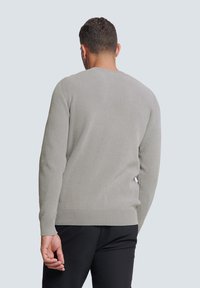 Grijze geribbelde trui met lange mouwen en een ronde hals, met een gestructureerde afwerking en nauwsluitende manchetten. Ggedragen met zwarte broek.