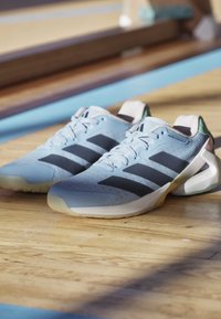 Hellblaue Sportschuhe mit schwarzen Streifen liegen auf einem Holzboden in der Turnhalle in der Nähe von blauen Spielfeldlinien.