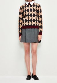 Maglione argyle in crema e nero con rifiniture bordeaux abbinato a una gonna plissettata grigia. La modella indossa mocassini neri.