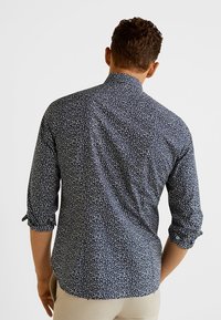 Marineblaues Hemd mit Knöpfen, weißem Blumenmuster, umgeschlagenen Ärmeln und einem Rückeneinsatz. Material aus Baumwollmischung mit glatter Textur.
