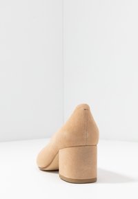 Beige mockakänga med blockklack, rund tå och slät yta, med en något texturerad baksida och en stadig, låg klack.