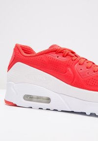 Sneakers Nike Air Max rouge et blanc avec semelle à coussin d'air visible et tige perforée pour la respirabilité, présentées de côté.
