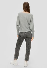 Hellgrauer gerippter Pullover mit weitem Ausschnitt, kombiniert mit hoch geschnittenen schwarzen Jeans und weißen klobigen Sneakern.