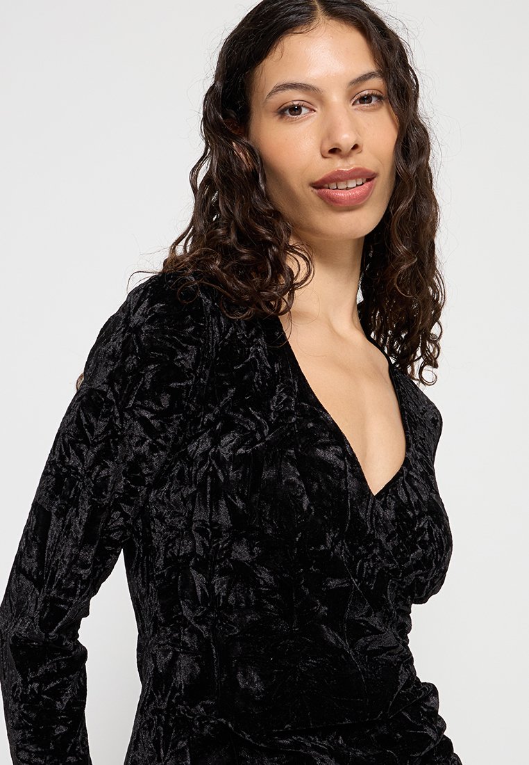 Schwarzes Samtkleid mit tiefem V-Ausschnitt, langen Ärmeln und strukturierten floralem Mustern, das ein reiches und luxuriöses Aussehen schafft.