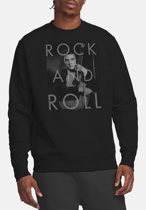 Mann trägt schwarzen Sweatshirt mit einem schwarz-weißen Foto eines Gitarristen und dem Text "ROCK AND ROLL" auf der Vorderseite.
