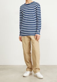 Blau-weiß gestreiftes Langarmshirt kombiniert mit beigen, lockeren Hosen und weißen Sneakers, mit einem entspannten Design und weichem Material.