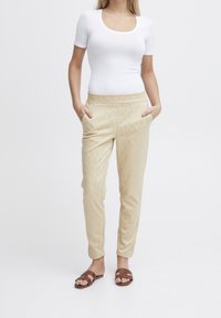 Beżowe wzorzyste spodnie z elastycznym pasem i bocznymi kieszeniami, połączone z dopasowanym białym topem z krótkim rękawem i brązowymi sandałami.