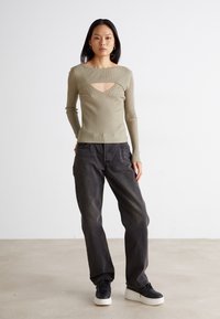 Ribbad långärmad tröja i olivgrön med en djup halsringning; tillsammans med lösa mörkgrå jeans och svarta sneakers. Minimalistisk design.