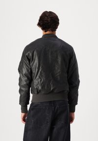 Černá kožená bomber bunda s žebrovanými manžetami a spodním lemem, vybavená zipem vpředu a bočními kapsami. Hladká textura s klasickým střihem.